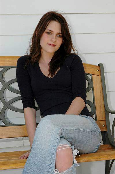 Kristen Stewart sits on a bench in torn jeans and black t-shirt