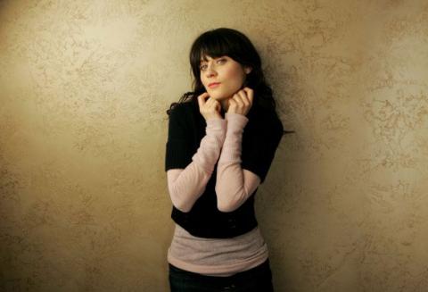 Zooey Deschanel - that's the cutie I like in peach and black sweater leaning up against gold print wallpaper